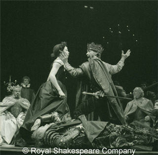 A black and white photo of performers in period costumes on a stage. A black and white photo of performers in period costumes on a stage.