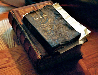 An old black leatherbound Bible atop a larger brown leatherbound book. An old black leatherbound Bible atop a larger brown leatherbound book.