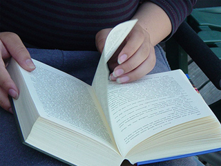 A book, open-faced, in a woman's lap, her hand turning the page. A book, open-faced, in a woman's lap, her hand turning the page.