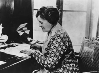 Photograph of Edith Wharton, writing while seated at a desk. Photograph of Edith Wharton, writing while seated at a desk.