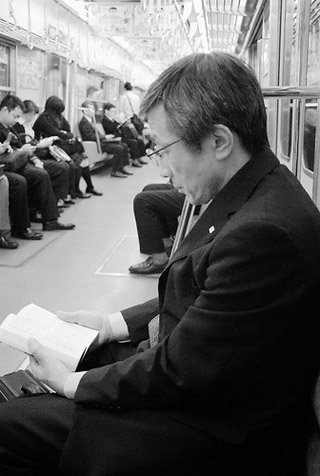 A man in a black coat sits on a subway and reads a book. A man in a black coat sits on a subway and reads a book.