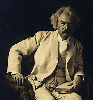 Photo of Mark Twain seated with a book in one hand. Photo of Mark Twain seated with a book in one hand.