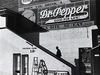 A black and white photograph showing a man walking up the steps to a movie theater with a separate entrance for African Americans. A black and white photograph showing a man walking up the steps to a movie theater with a separate entrance for African Americans.