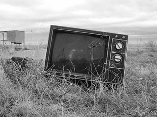 Black and white photo of a television abandoned in the dry prairie grass. Black and white photo of a television abandoned in the dry prairie grass.