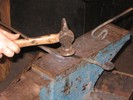 The twisted bar lies on the anvil face as a loop is made in one end of another bar.