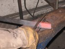 The two parallel arms of a spring fuller are applied to a glowing red bar.
