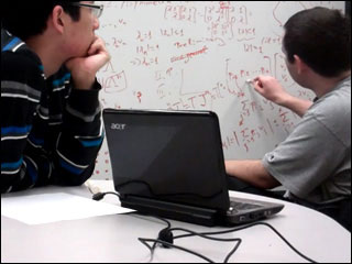 Two students working on a number of mathematical equations on a whiteboard. Two students working on a number of mathematical equations on a whiteboard.