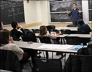 Male student in blue dress shirt in fron of black board and speaking to a small group of students. Male student in blue dress shirt in fron of black board and speaking to a small group of students.