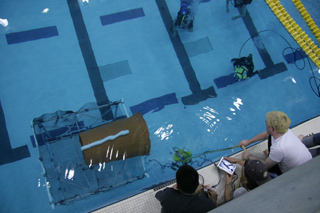 Students attempt to maneuver their robot into a garbage can anchored on its side on the bottom of the pool. Students attempt to maneuver their robot into a garbage can anchored on its side on the bottom of the pool.