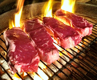 Four steaks on a charcoal grill with flames. Four steaks on a charcoal grill with flames.