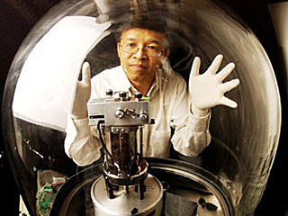 A man wearing white latex gloves posing both hands on a glass chamber containing a mechanical device. A man wearing white latex gloves posing both hands on a glass chamber containing a mechanical device.