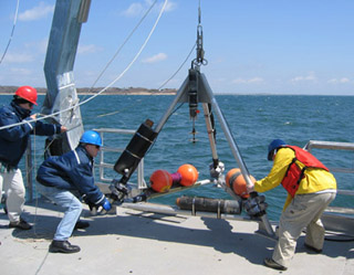 Three people winching large tripod off deck into ocean. Three people winching large tripod off deck into ocean.