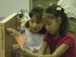 A photo of two girls creating a path for a falling ball on a peg board. A photo of two girls creating a path for a falling ball on a peg board.