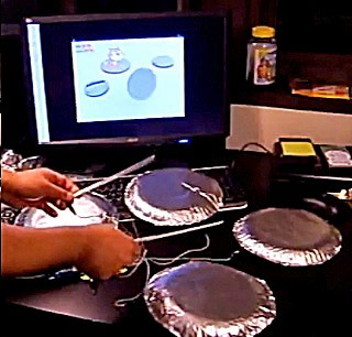 Photo showing hands playing four foil “drums” wired to a computer, with the Scratch cat character animated on screen. Photo showing hands playing four foil “drums” wired to a computer, with the Scratch cat character animated on screen.
