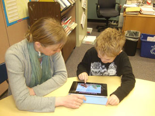 A photo of an autistic boy using an iPad with his teacher. A photo of an autistic boy using an iPad with his teacher.