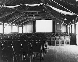 A black and white photo of movie hall with rows of wodden chairs. A black and white photo of movie hall with rows of wodden chairs.