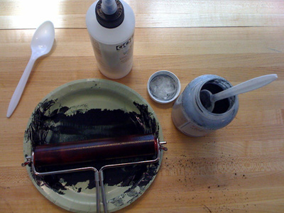 Photo of black paint on a plate, with roller, and a couple of containers.