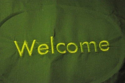 Photo of fabric embroidered with the word Welcome in a Helvetica-style font.