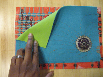 Photo of circular LilyPad device in some fabric, layed on top of grid-covered fabric.