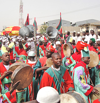 Photo of many people gathered in a street, with large loudspeakers, hand drums, and a hand holding up a tape recorder. Photo of many people gathered in a street, with large loudspeakers, hand drums, and a hand holding up a tape recorder.