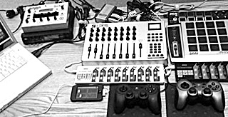 A photo of laptop computer, mixing board, iPod, two joystick controllers and several other electronic music devices arranged on a tabletop. A photo of laptop computer, mixing board, iPod, two joystick controllers and several other electronic music devices arranged on a tabletop.