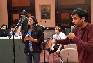 Photo of two singers on microphones, with a recording engineer standing in the background monitoring the session on a laptop. Photo of two singers on microphones, with a recording engineer standing in the background monitoring the session on a laptop.