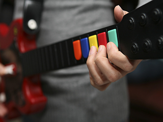 A person playing a Guitar Hero controller that looks like a red electric guitar with multi-colored buttons instead of strings. A person playing a Guitar Hero controller that looks like a red electric guitar with multi-colored buttons instead of strings.
