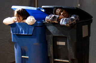 The heads of two people peek out from the top of garbage bins. The heads of two people peek out from the top of garbage bins.