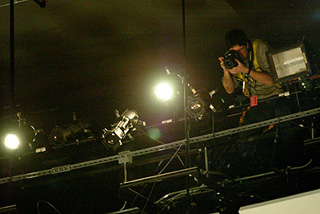 A photographer perched on a catwalk above a stage. A photographer perched on a catwalk above a stage.