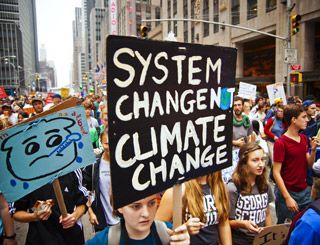 In the midst of a crowd, a young woman holds a sign with the words: System Change. Not Climate Change. In the midst of a crowd, a young woman holds a sign with the words: System Change. Not Climate Change.