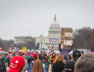 A photo of a young girl in a crowd of people holding up a sign that reads 'Too young to vote, old enough to care' during the 2017 Women's March on Washington. A photo of a young girl in a crowd of people holding up a sign that reads 'Too young to vote, old enough to care' during the 2017 Women's March on Washington.