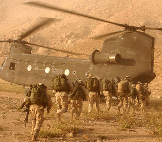 A group of U.S. soldiers run in a desert dressed in tan fatigues towards a large waiting helicopter. A group of U.S. soldiers run in a desert dressed in tan fatigues towards a large waiting helicopter.