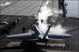 Image depicts an aircraft and navy personnel on the deck of an aircraft carrier. Image depicts an aircraft and navy personnel on the deck of an aircraft carrier.