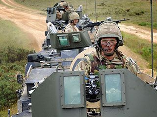 A group of men, each wearing military gear, drive armoured vehicles down a dirt road. A group of men, each wearing military gear, drive armoured vehicles down a dirt road.