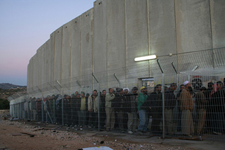 Daybreak, line of people behind a fence adjacent to cement wall. Daybreak, line of people behind a fence adjacent to cement wall.