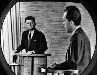 The grainy image on a television screen shows John F. Kennedy and Richard Nixon standing at podiums. The grainy image on a television screen shows John F. Kennedy and Richard Nixon standing at podiums.