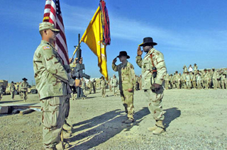 Assembled soldiers salute a flag in a desert setting. Assembled soldiers salute a flag in a desert setting.