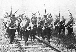 Photograph of a group of soldiers, rifles slung over their shoulders, marching along a railroad track. Photograph of a group of soldiers, rifles slung over their shoulders, marching along a railroad track.