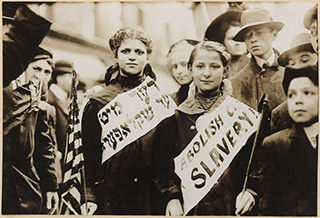 A photo from 1909 of two girls wearing banners that read "ABOLISH CHILD SLAVERY!" in English and Yiddish. A photo from 1909 of two girls wearing banners that read "ABOLISH CHILD SLAVERY!" in English and Yiddish.