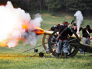 A photograph of a group of people, dressed in Civil War uniforms, standing by a cannon. The cannon has just gone off. A photograph of a group of people, dressed in Civil War uniforms, standing by a cannon. The cannon has just gone off.