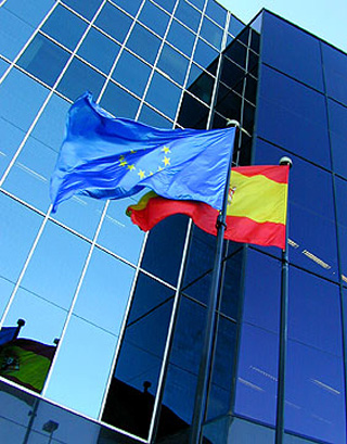 Flags of the European Union and Spain wave outside an office building. Flags of the European Union and Spain wave outside an office building.