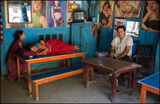 Tiwali sits across from a woman watching TV and another napping at a small colorful tea shop. Tiwali sits across from a woman watching TV and another napping at a small colorful tea shop.