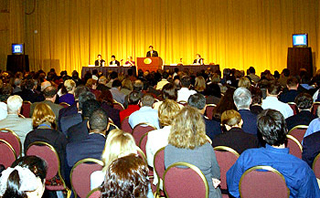Photograph of speaker presenting to a large audience. Photograph of speaker presenting to a large audience.