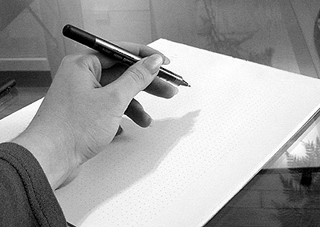 Black and white photo of a hand holding a pen, prepared to write on a sheet of paper. Black and white photo of a hand holding a pen, prepared to write on a sheet of paper.