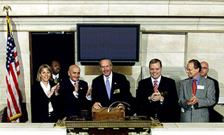 Seven people standing in front of the podium above the trading floor of the New York Stock Exchange. Seven people standing in front of the podium above the trading floor of the New York Stock Exchange.