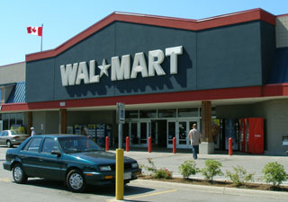 A small blue car is parked in front of a Wal-Mart entrance. A small blue car is parked in front of a Wal-Mart entrance.