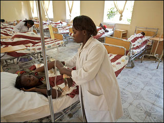 Woman standing over another lying in a hospital bed next to an IV drip. Woman standing over another lying in a hospital bed next to an IV drip.