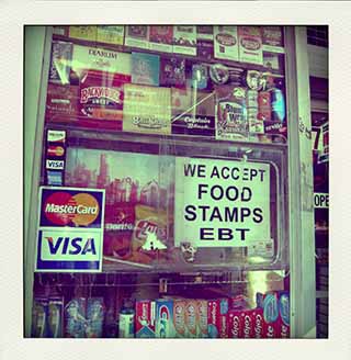 A deli window in Brooklyn with a sign that reads "We accept food stamps and EBT". A deli window in Brooklyn with a sign that reads "We accept food stamps and EBT".