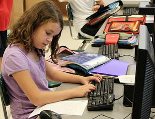 A young girl in a lilac shirt sits at a computer working on homework. A young girl in a lilac shirt sits at a computer working on homework.