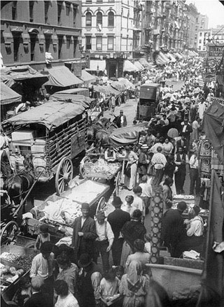 A black and white photo of an urban street crowded with people, wagons, carts, and horses. A black and white photo of an urban street crowded with people, wagons, carts, and horses.